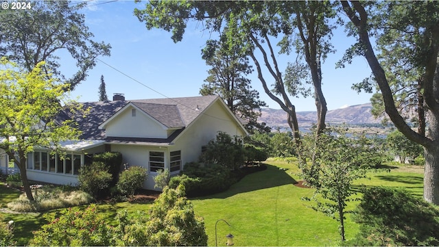 view of property exterior with a lawn, a mountain view, and a sunroom