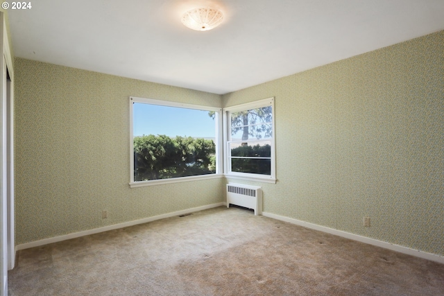 empty room featuring light carpet and radiator heating unit