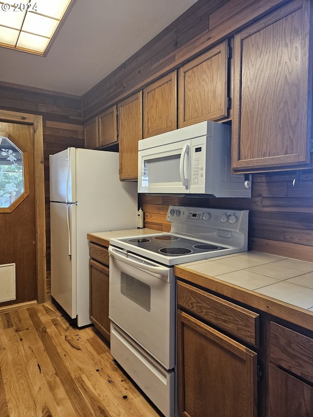 kitchen featuring light hardwood / wood-style floors, white appliances, tile counters, and wooden walls