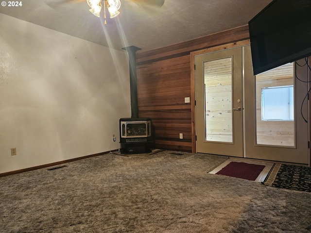 unfurnished living room featuring a wood stove, wooden walls, and carpet floors