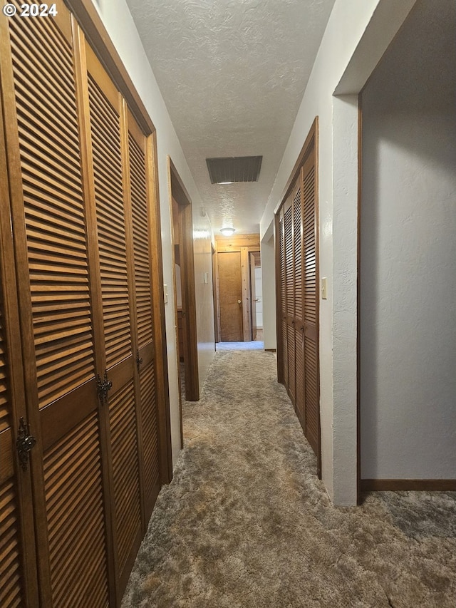 hall featuring dark carpet and a textured ceiling