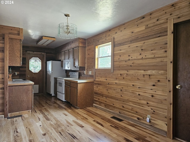 kitchen featuring white appliances, pendant lighting, wooden walls, light hardwood / wood-style floors, and sink