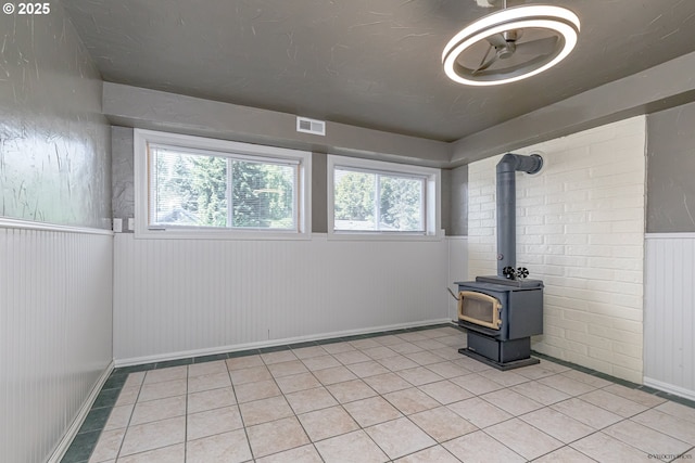 1504 SW 24th St, Troutdale, OR 97060 - unfurnished living room with light tile patterned flooring, a wainscoted wall, a wood stove, healthy amount of natural light, and baseboards