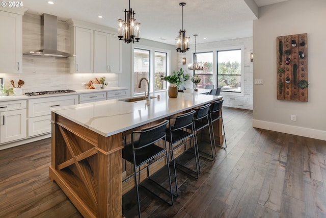 kitchen featuring white cabinetry, a breakfast bar area, wall chimney exhaust hood, and a center island with sink