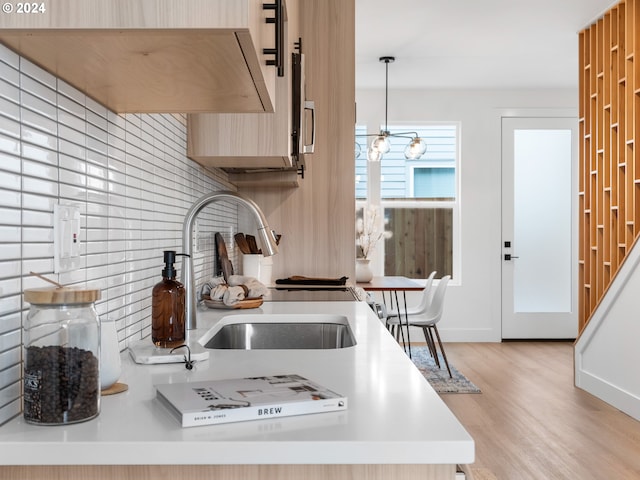 kitchen featuring decorative backsplash, light wood-type flooring, sink, an inviting chandelier, and hanging light fixtures