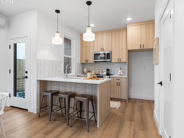 kitchen with kitchen peninsula, light brown cabinetry, light wood-type flooring, and sink