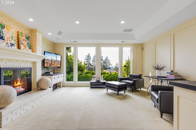 living room with a raised ceiling, a brick fireplace, plenty of natural light, and light carpet