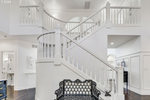 staircase featuring ornamental molding, a high ceiling, and wood-type flooring