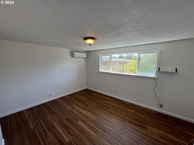 empty room with dark hardwood / wood-style flooring, a wall mounted air conditioner, and a textured ceiling