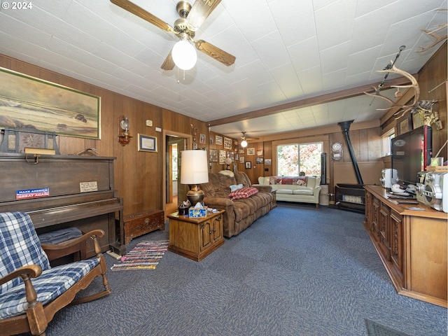 carpeted living room with ceiling fan, a wood stove, beam ceiling, and wooden walls