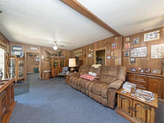 carpeted living room featuring ceiling fan, beam ceiling, and wooden walls