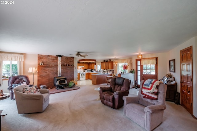 living room with light carpet, a wood stove, ceiling fan, and a healthy amount of sunlight