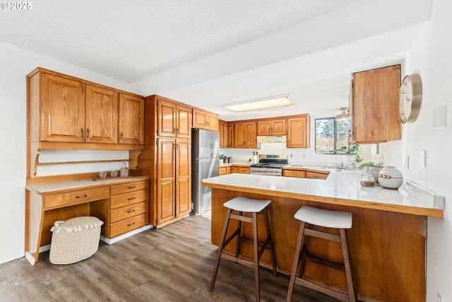 kitchen featuring a kitchen breakfast bar, kitchen peninsula, stainless steel appliances, a textured ceiling, and light hardwood / wood-style flooring