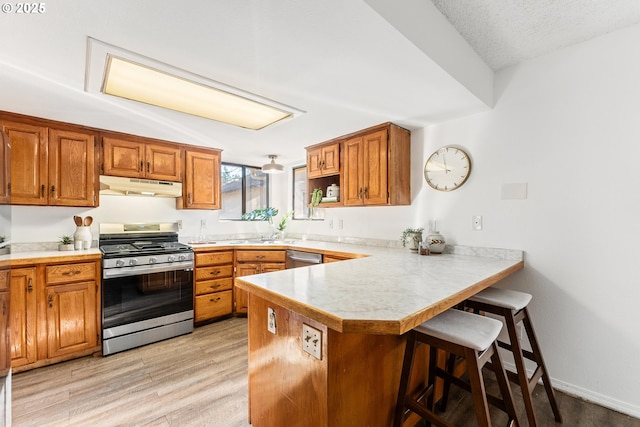 kitchen with a textured ceiling, light wood-type flooring, appliances with stainless steel finishes, a kitchen breakfast bar, and kitchen peninsula