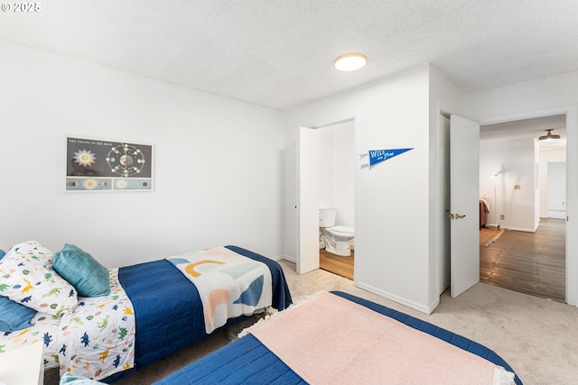 bedroom with ensuite bath, carpet flooring, and a textured ceiling