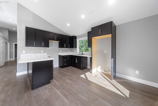 kitchen featuring sink, light stone countertops, a kitchen bar, light wood-type flooring, and high vaulted ceiling