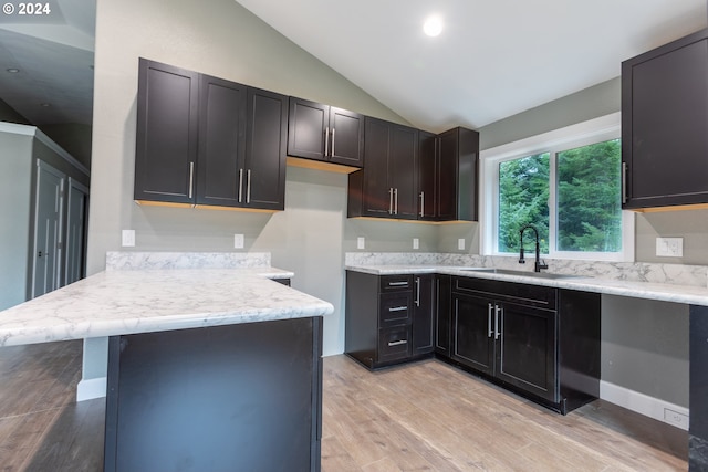 kitchen with light hardwood / wood-style floors, sink, a kitchen breakfast bar, and vaulted ceiling