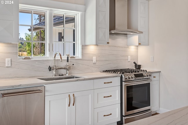 kitchen with light stone counters, sink, wall chimney range hood, and stainless steel appliances