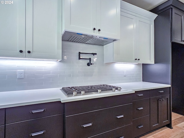 kitchen with stainless steel gas stovetop, decorative backsplash, white cabinetry, and light hardwood / wood-style floors