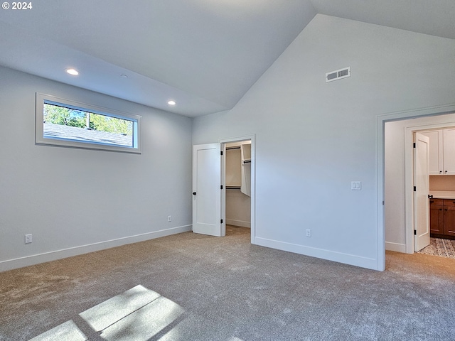 unfurnished bedroom with a spacious closet, connected bathroom, high vaulted ceiling, and light carpet