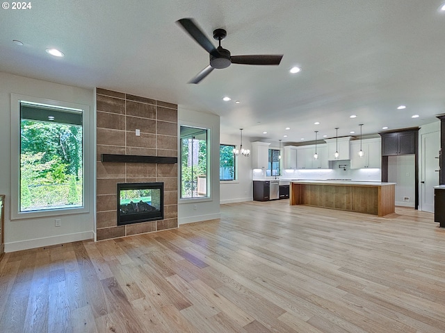 unfurnished living room with ceiling fan with notable chandelier, a textured ceiling, light wood-type flooring, and a tile fireplace