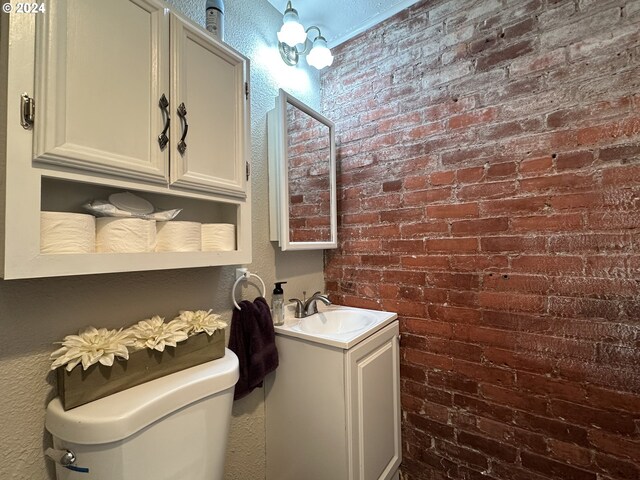 bathroom featuring vanity, brick wall, and toilet