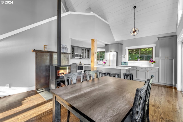 dining space featuring wooden ceiling, wood-type flooring, a wood stove, and high vaulted ceiling