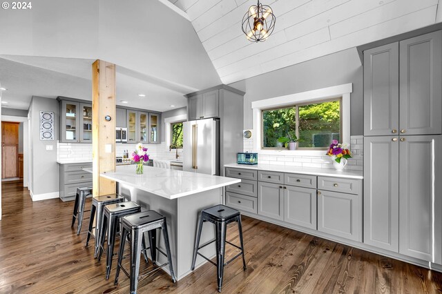 kitchen with a center island, dark wood-type flooring, vaulted ceiling, backsplash, and appliances with stainless steel finishes