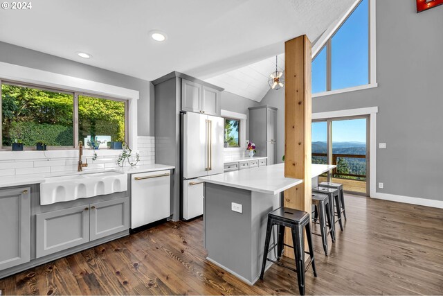 kitchen with a breakfast bar, white appliances, gray cabinets, dark hardwood / wood-style floors, and sink