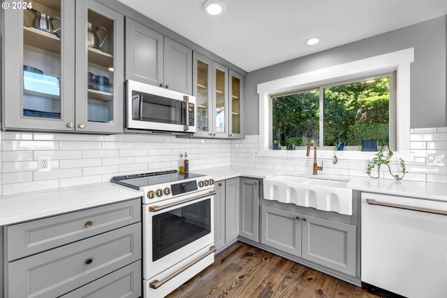 kitchen with backsplash, dark hardwood / wood-style floors, white appliances, and gray cabinetry