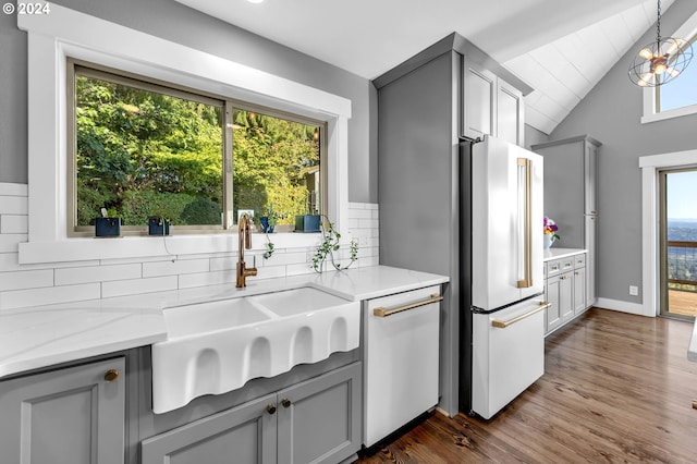 kitchen with sink, vaulted ceiling, white appliances, and gray cabinetry