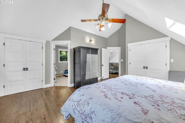 bedroom with ceiling fan, multiple closets, vaulted ceiling with skylight, and dark wood-type flooring