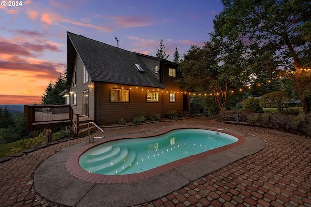 pool at dusk with a wooden deck and a patio area