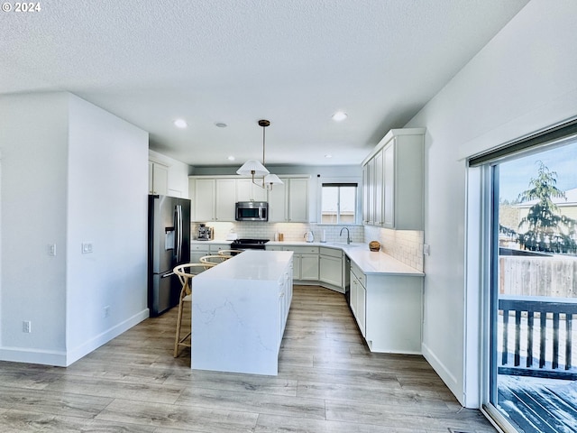 kitchen with a kitchen island, appliances with stainless steel finishes, light hardwood / wood-style flooring, sink, and decorative light fixtures