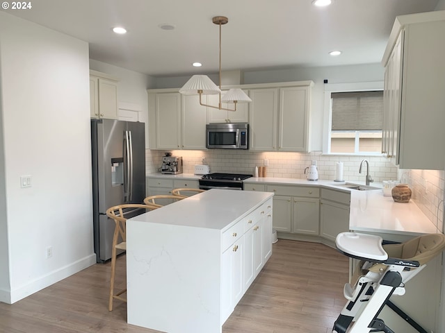 kitchen featuring white cabinets, a kitchen island, pendant lighting, light hardwood / wood-style floors, and stainless steel appliances