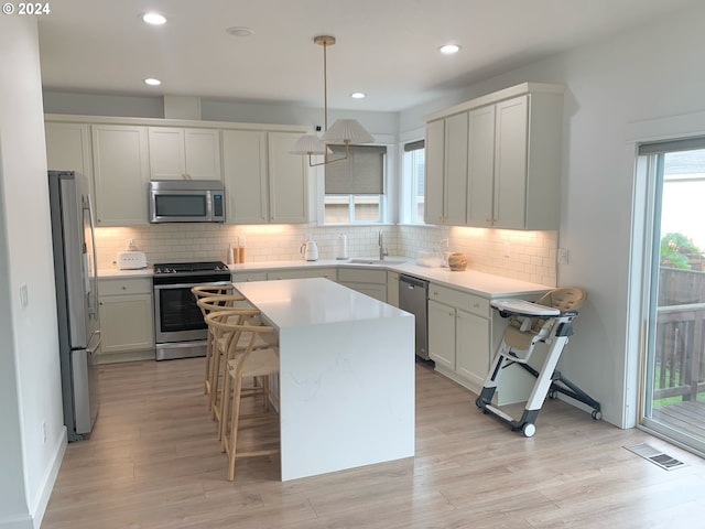 kitchen featuring hanging light fixtures, appliances with stainless steel finishes, a breakfast bar, light wood-type flooring, and a center island