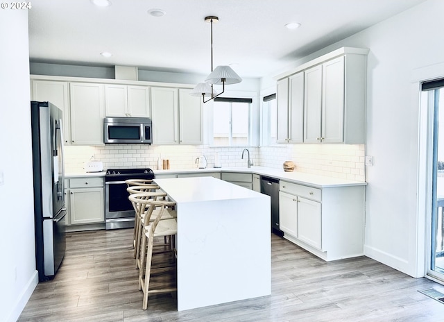 kitchen with a kitchen island, appliances with stainless steel finishes, hanging light fixtures, and white cabinetry