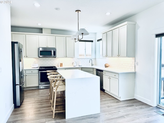 kitchen featuring appliances with stainless steel finishes, a kitchen bar, a kitchen island, white cabinetry, and pendant lighting