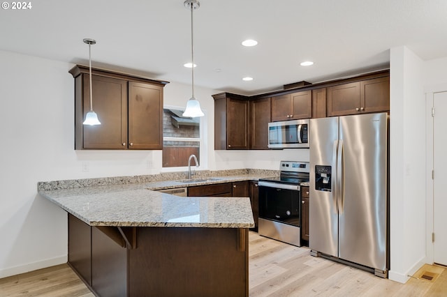 kitchen with sink, appliances with stainless steel finishes, pendant lighting, and light wood-type flooring