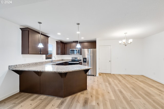 kitchen with kitchen peninsula, sink, decorative light fixtures, light wood-type flooring, and appliances with stainless steel finishes