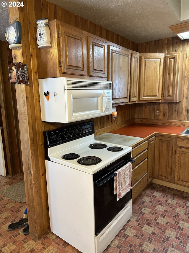 kitchen with wood walls, white appliances, and a textured ceiling