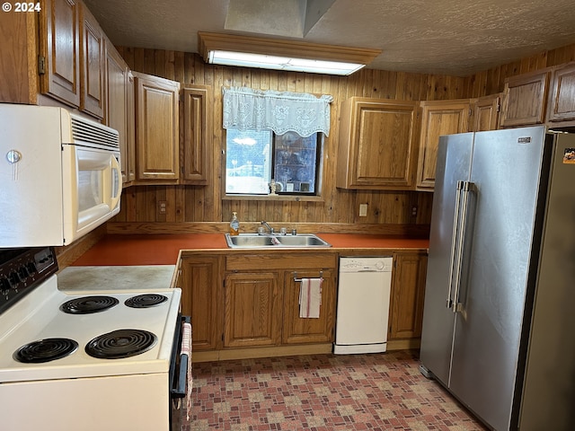 kitchen with white appliances, wooden walls, sink, and a textured ceiling