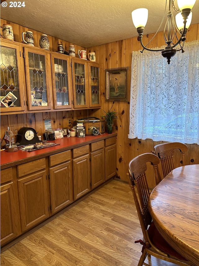 dining area with wood walls, light wood-type flooring, a textured ceiling, and a notable chandelier