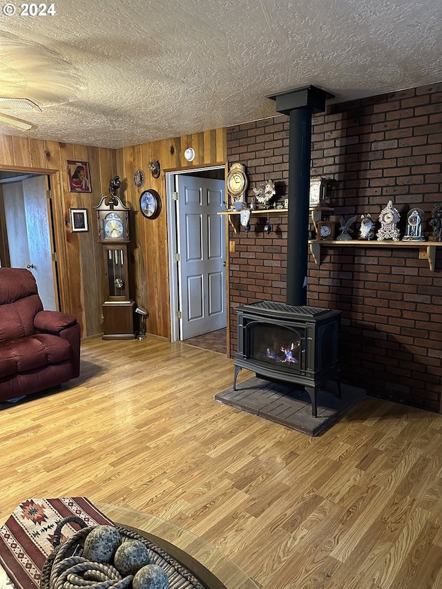 living room with wood walls, hardwood / wood-style flooring, a textured ceiling, and a wood stove