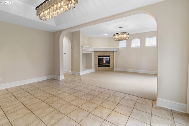 unfurnished living room featuring a tiled fireplace, light tile patterned floors, and a chandelier