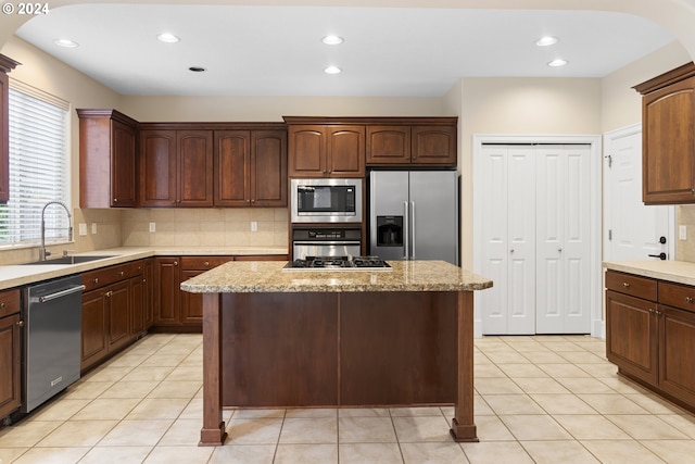 kitchen featuring stainless steel appliances, a kitchen island, sink, and light stone counters