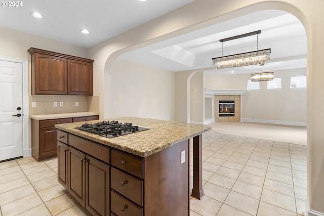 kitchen with light tile patterned floors, backsplash, a kitchen island, a tiled fireplace, and stainless steel gas stovetop