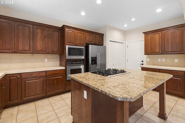 kitchen featuring appliances with stainless steel finishes, backsplash, light stone countertops, a kitchen island, and light tile patterned flooring