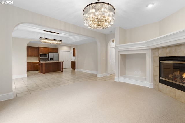 unfurnished living room featuring a tile fireplace, light carpet, and a notable chandelier