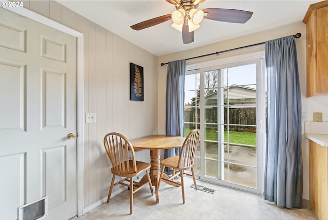 dining area with ceiling fan and wooden walls